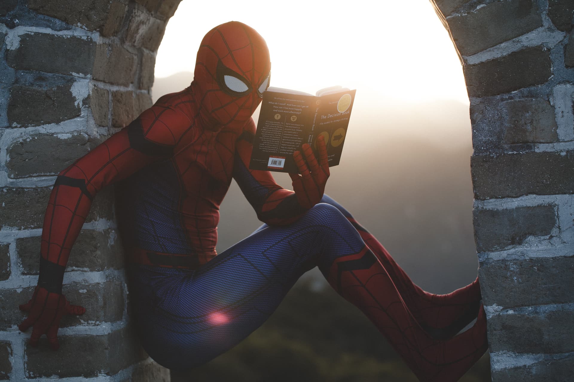 Spider-man reading a comic book while climbing a brick wall